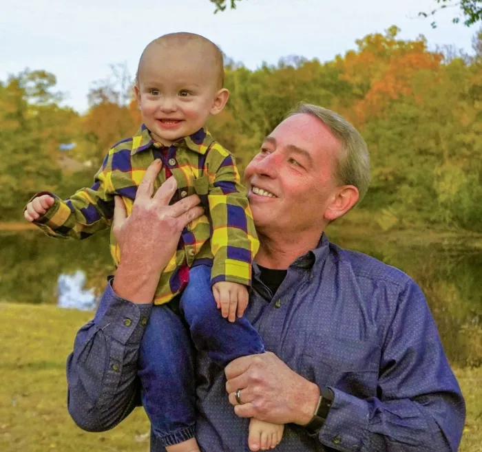 Todd Hayes holding his youngest son outdoors in the fall